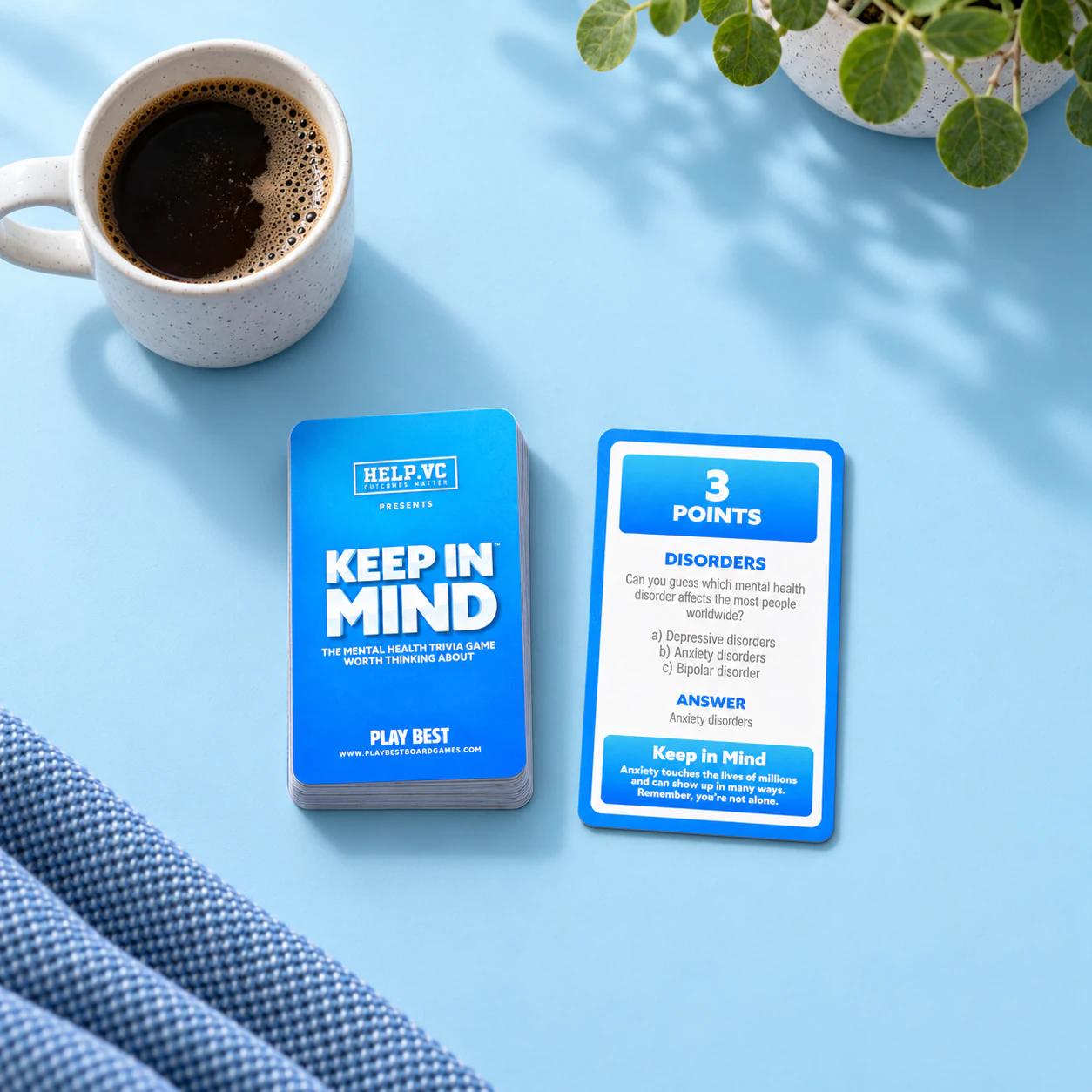 Illustrative product scene showing the HELP.VC branded Keep in Mind box and blue question card beside a mug